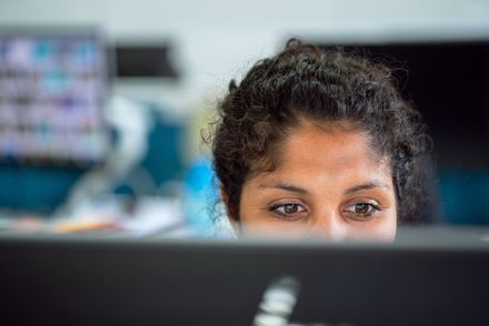 Eine junge Frau ist über dem Rand eines Computerbildschirms zu sehen, sie schaut konzentriert auf den Bildschirm.