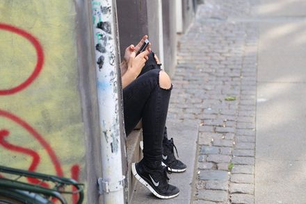 Das Foto zeigt ein Mädchen mit Handy, das alleine in einem Hauseingang sitzt.